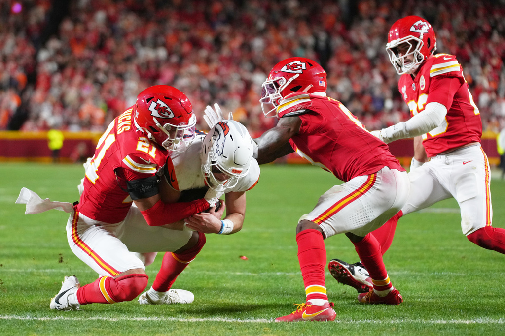 Denver Broncos quarterback Bo Nix, center, pushes through across the goal line to score on a run as Kansas City Chiefs safety Jaden Hicks (21), cornerback Kristian Fulton, second from right, and linebacker Drue Tranquill, right, try to stop him during the second half of an NFL football game Thursday, Dec. 25, 2025, in Kansas City. (AP Photo/Ed Zurga)
