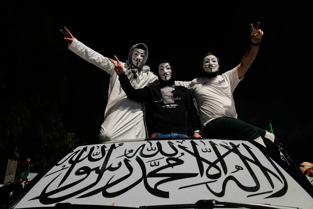 Syrian men wearing anonymous masks flash victory signs, as they stand on top of their car with its front window covered by an Islamic flag, during celebrations marking the first anniversary of the ousting of the Bashar Assad regime in Damascus, Sunday, Dec. 7, 2025. (AP Photo/Hussein Malla)