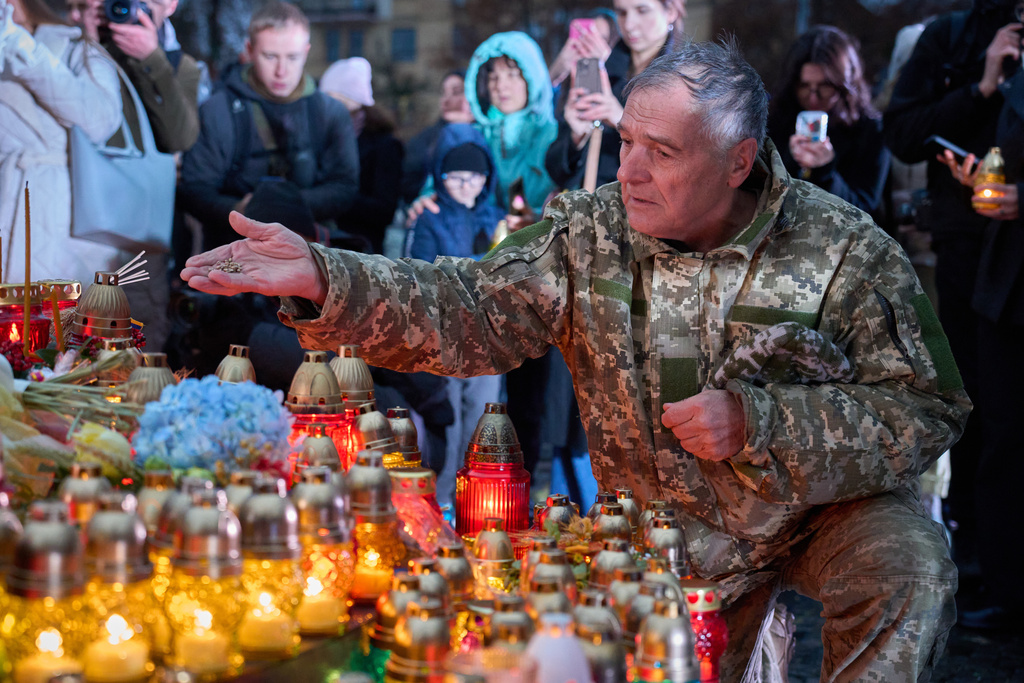 A war veteran throws seeds at the foot of the monument to victims of Holodomor, the Great Famine, which took place in the 1930's and that killed millions, during annual commemorating ceremony in Kyiv, Ukraine, Saturday, Nov. 22, 2025. (AP Photo/Efrem Lukatsky)