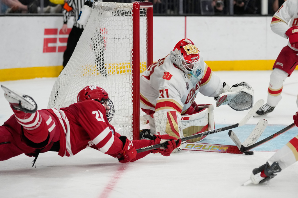 Wisconsin forward Ryan Botterill (21) dives to attempt a shot on Denver goaltender Johnny Hicks (31) in the second period of the championship game at the NCAA Frozen Four men's college hockey tournament Saturday, April 11, 2026, in Las Vegas. (AP Photo/John Locher)