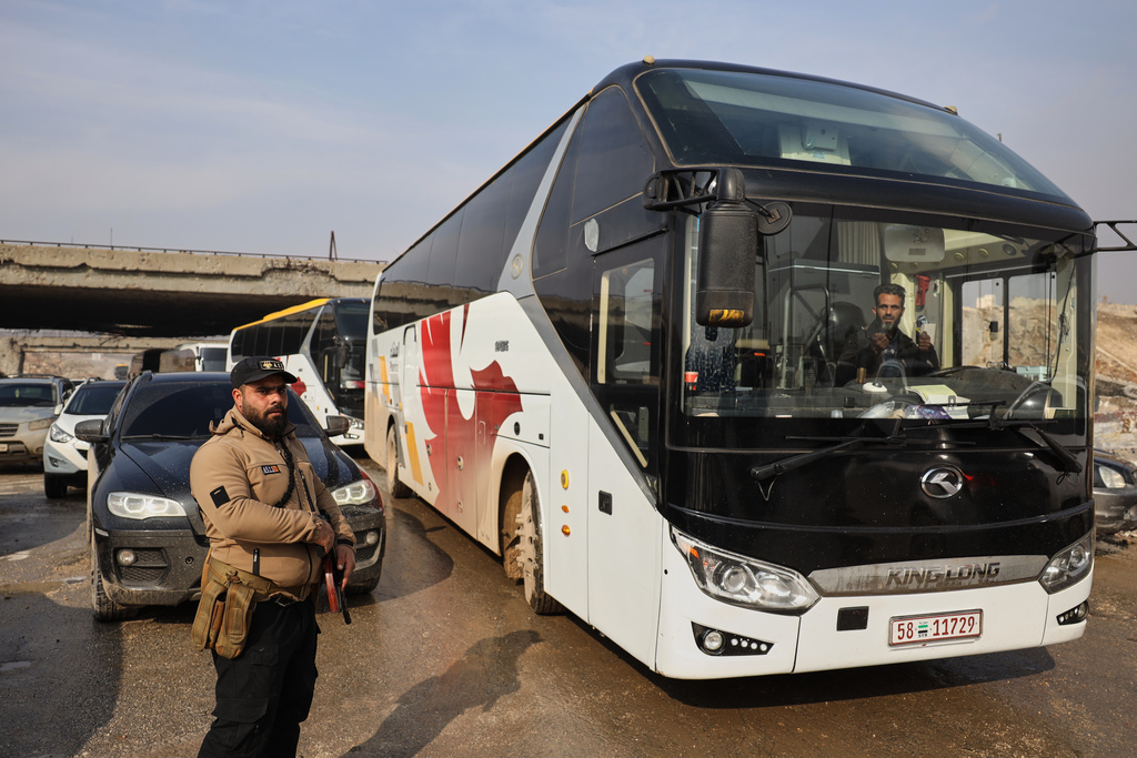 Members of Syrian government forces stand around buses prepared to evacuate Kurdish militants, under escort to the country's northeast, controlled by the SDF, after a ceasefire was announced following days of clashes in the northern city of Aleppo, Syria, Friday, Jan. 9, 2026. (AP Photo/Omar Albam)