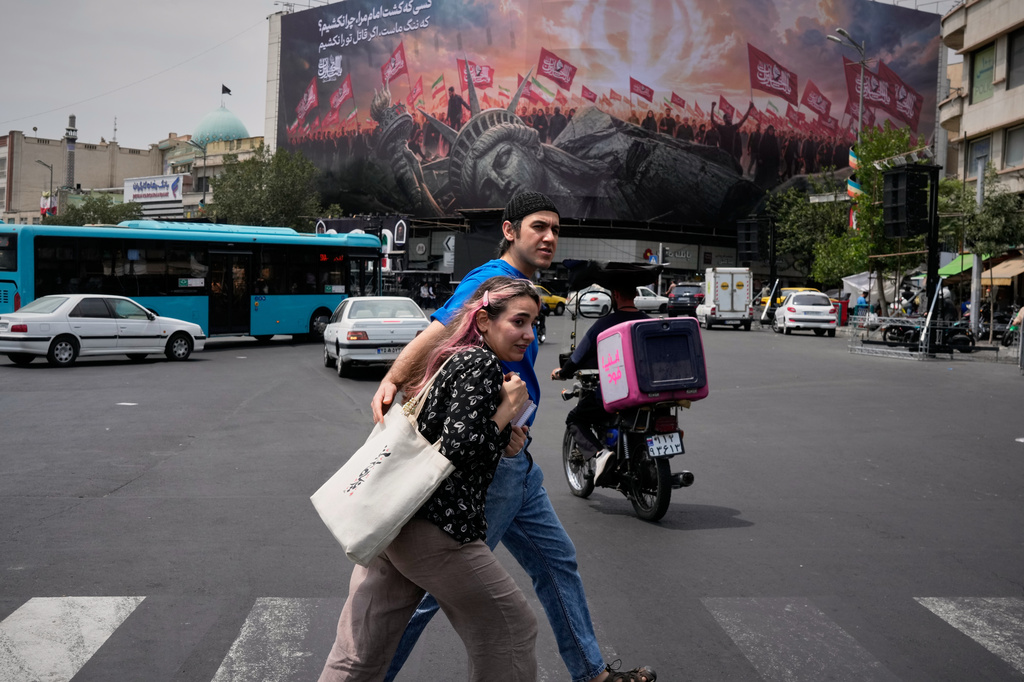 Pedestrians cross a street in front of a billboard depicting a fallen Statue of Liberty and crowds carrying Iranian and Shiite flags at Revolution Square in Tehran, Iran, Monday, Aug. 3, 2026. (AP Photo/Vahid Salemi)