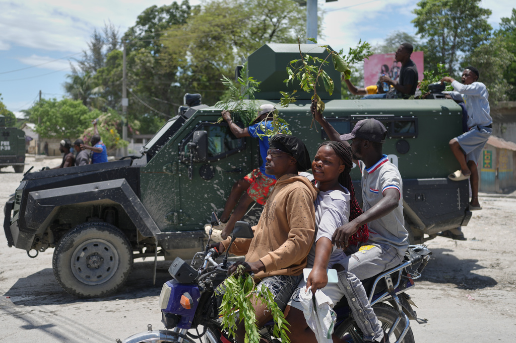 Residents of Cité Soleil celebrate the arrival of armored police vehicles during a protest to demand that police officers go and fight the gangs that control their neighborhood, in Port-au-Prince, Haiti, Tuesday, May 12, 2026. (AP Photo/Odelyn Joseph)