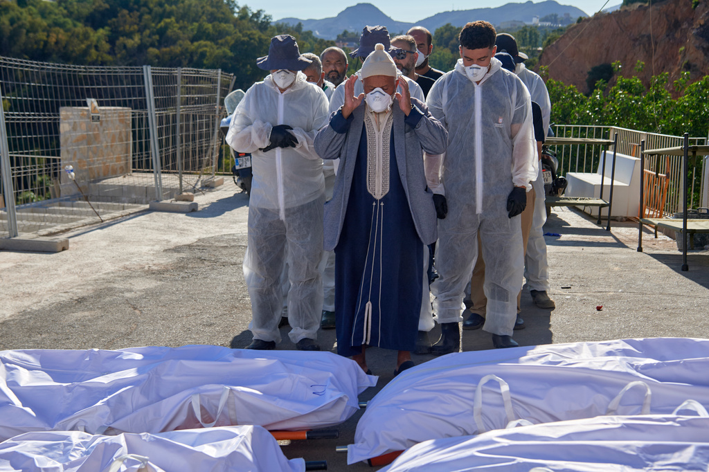 A man, accompanied by funeral workers, prays over bodies of migrants who died while trying to cross from Morocco into the Spanish exclave of Ceuta, Friday, Aug. 21, 2026. (AP Photo/Antonio Sempere)