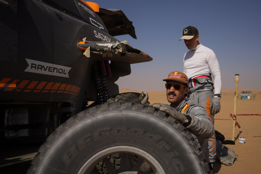 Driver Guillaume de Mevius and co-driver Mathieu Baumel change a tire of their car at the end of the ninth stage of the Dakar Rally between Wadi Ad Dawasir and Bisha, Saudi Arabia, Tuesday, Jan.13, 2026. (AP Photo/Thibault Camus)