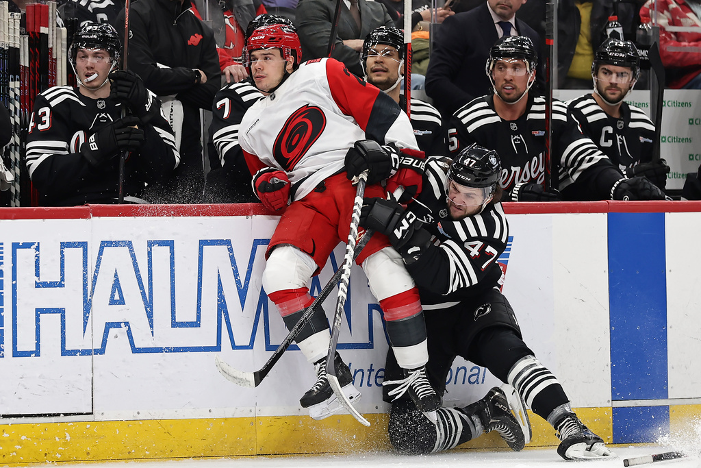 New Jersey Devils left wing Paul Cotter (47) checks Carolina Hurricanes center Sebastian Aho (20) in front of the Devils bench during the first period of an NHL hockey game Saturday, Jan. 17, 2026, in Newark, N.J. (AP Photo/Adam Hunger)