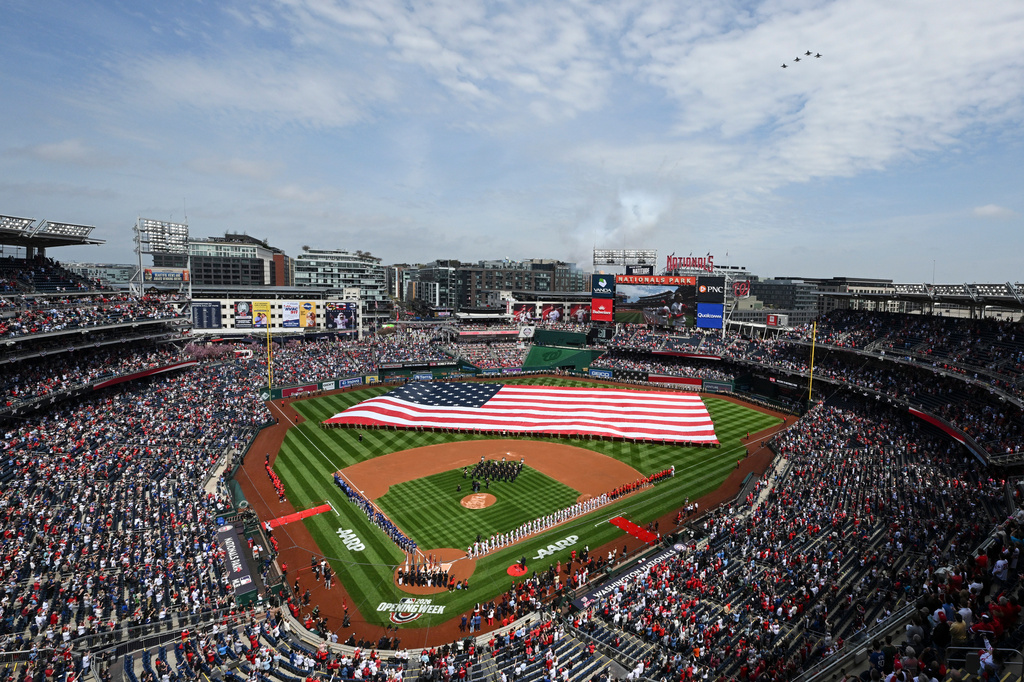 An American flag is held across the field during the national anthem as F-16C Fighting Falcons flyover before the Washington Nationals home-opener baseball game against the Los Angeles Dodgers, Friday, April 3, 2026, in Washington. (AP Photo/Terrance Williams)