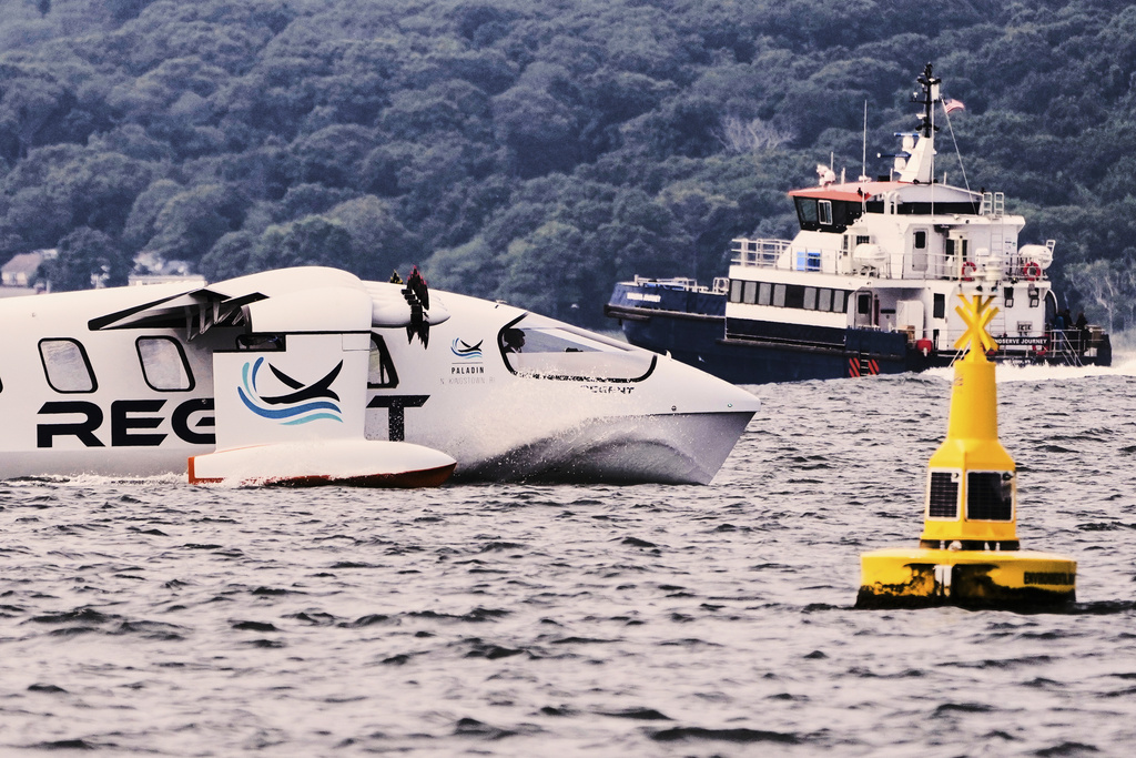 The REGENT Viceroy Seaglider, a winged passenger ferry, passes a navigation buoy and a ship during a test run on Narragansett Bay, Wednesday, Aug. 6, 2025, off the coast of North Kingstown, R.I. (AP Photo/Charles Krupa)