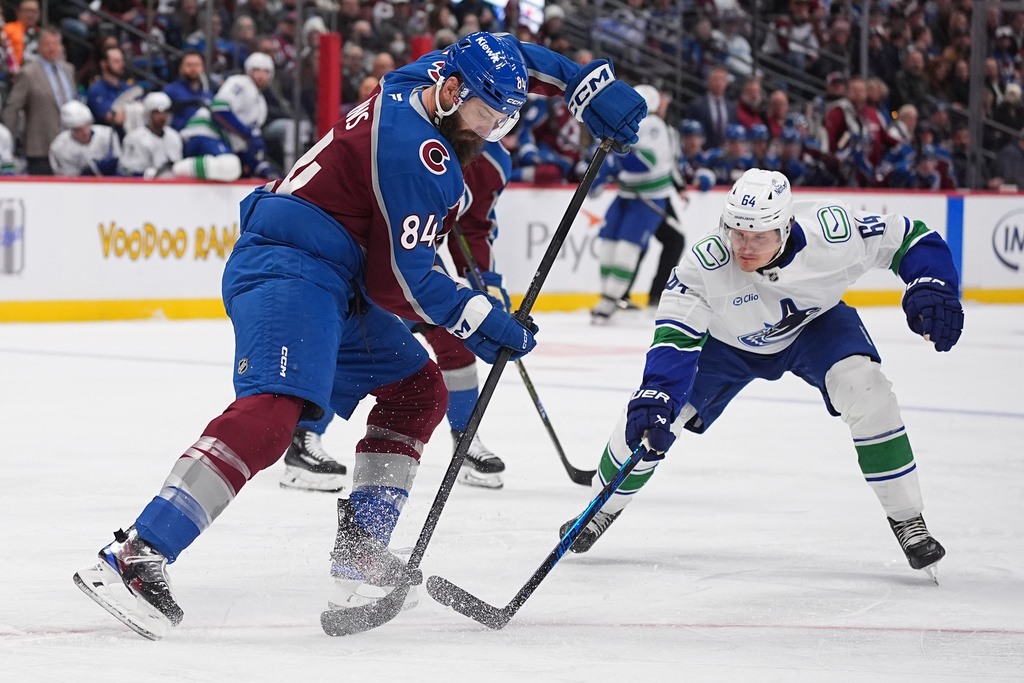 Colorado Avalanche defenseman Brent Burns, left, clears the puck as Vancouver Canucks center David Kampf defends in the second period of an NHL hockey game, Tuesday, Dec. 2, 2025, in Denver. (AP Photo/David Zalubowski)