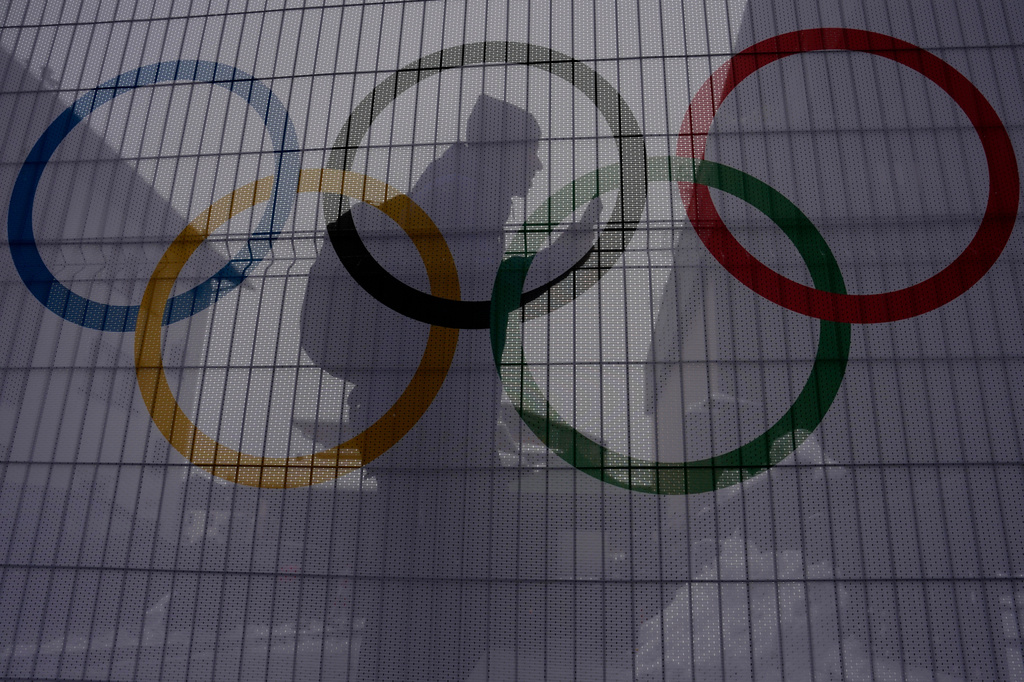 A person walks past Olympic rings on net covered fences at the 2026 Winter Olympics, in Bormio, Italy, Wednesday, Feb. 4, 2026. (AP Photo/John Locher)