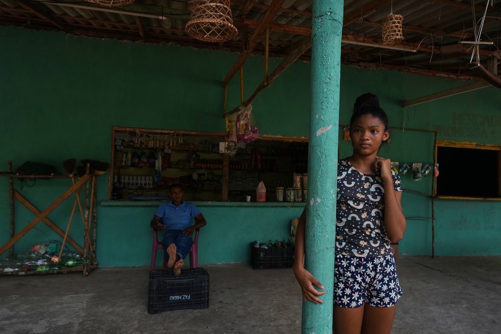 A girl stands next to her father in a grocery shop in Itacoa Miri, Brazil, Tuesday, Nov. 18, 2025. (AP Photo/Fernando Llano)