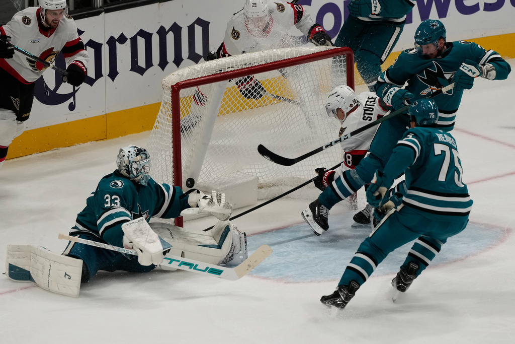 Ottawa Senators center Tim Stützle (18) scores a goal past San Jose Sharks goaltender Alex Nedeljkovic (33), center Nick Cousins, top right, and right wing Ryan Reaves during the third period of an NHL hockey game in San Jose, Calif., Saturday, Nov. 22, 2025. (AP Photo/Jeff Chiu)