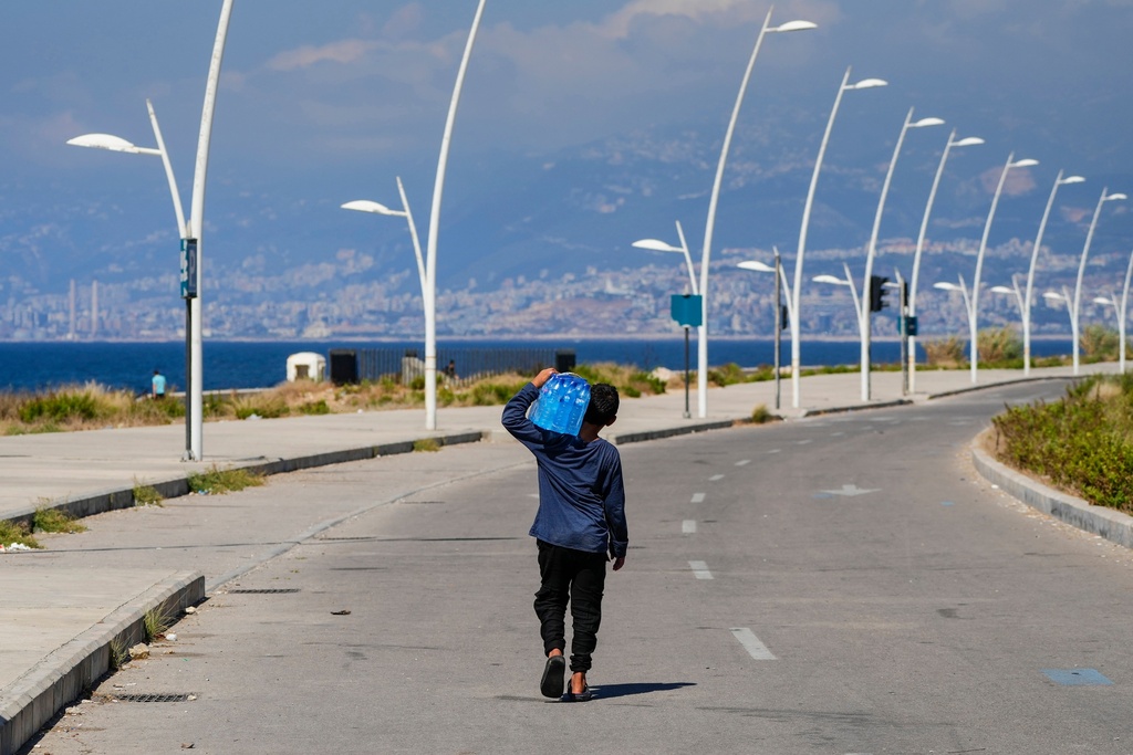 FILE - A young street vendor carries a pack of water bottles as he looking for customers during a sweltering day on the Mediterranean Sea corniche in Beirut, Lebanon, July 20, 2023. (AP Photo/Hassan Ammar, File)
