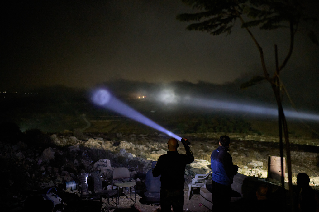 A Palestinian scans a valley with a flashlight as cars move on the top of a hill during a volunteer night watch to help prevent Israeli settler attacks in the West Bank town of Sinjil, Wednesday, Sept. 2, 2026. (AP Photo/Leo Correa)