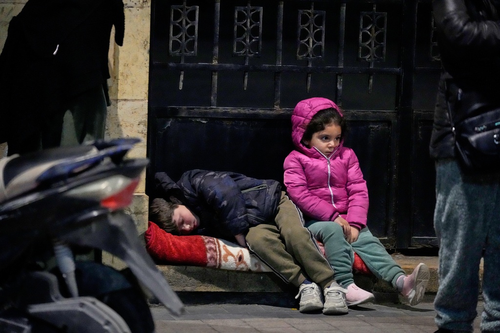 Children sit on a sidewalk as displaced families fleeing Israeli strikes in southern Lebanon arrive in the southern port city of Sidon, early Monday, March 2, 2026. (AP Photo/Mohammed Zaatari)