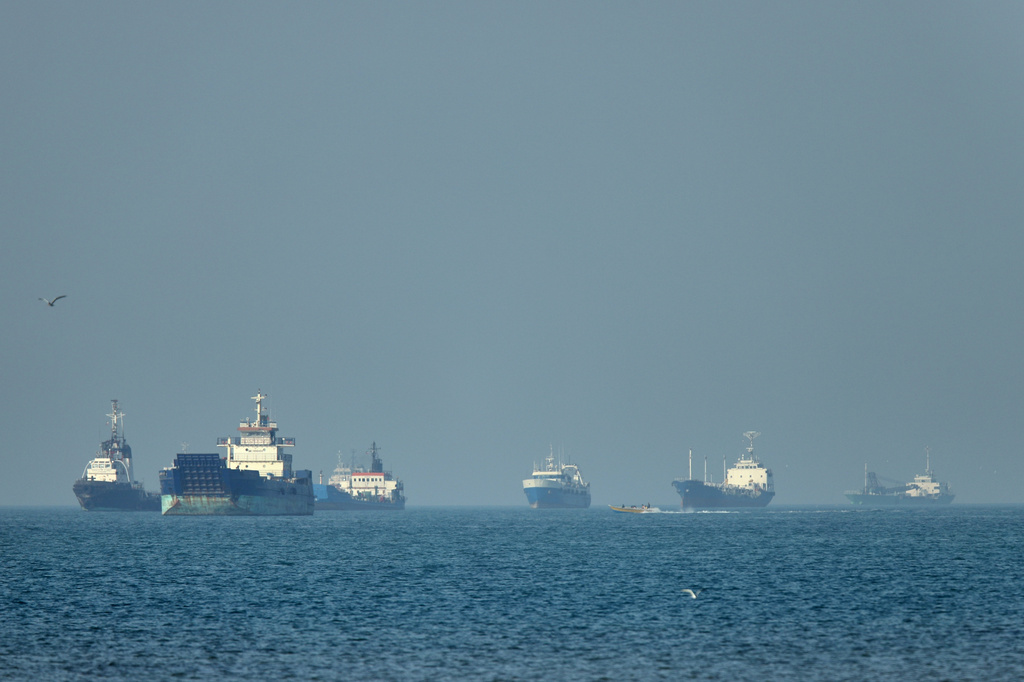 Cargo ships, including bulk carriers and general cargo vessels, sit at anchor offshore as a small motorboat passes in the foreground, in the Strait of Hormuz off Bandar Abbas, Iran, Monday, May 4 , 2026.(Amirhosein Khorgooi/ISNA via AP)