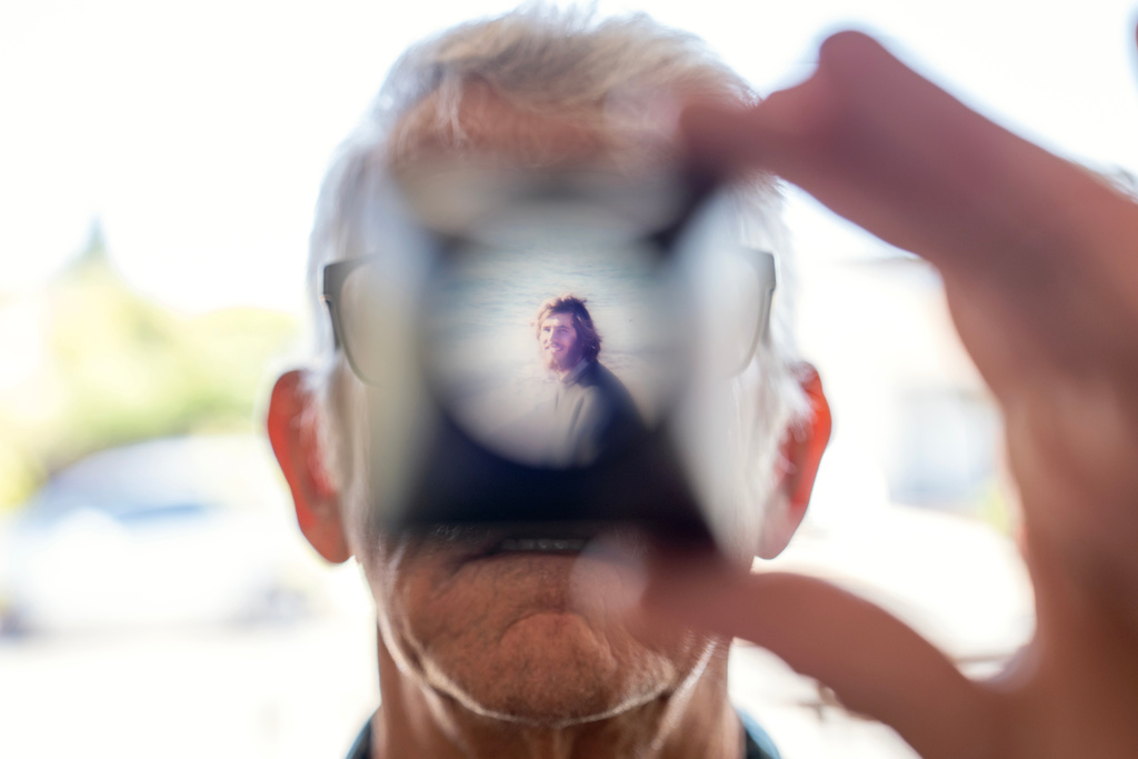 Christy Morrill, 72, who lost decades of memories to autoimmune encephalitis, holds up a viewfinder with a slide film of himself as a college student while looking through old photographs at his home, Wednesday, Aug. 20, 2025, in San Carlos, Calif. (AP Photo/David Goldman)