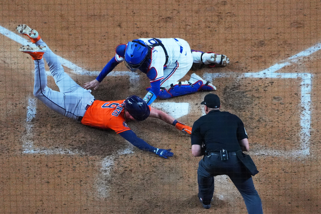 Houston Astros' Zach Dezenzo, left, slides in to score ahead of the tag by Texas Rangers catcher Danny Jansen, top, on a bunt by Astros' Christian Vázquez, not visible, as home plate umpire Paul Clemons looks on during the fifth inning of a baseball game Monday, May 25, 2026, in Arlington, Texas. (AP Photo/Julio Cortez)