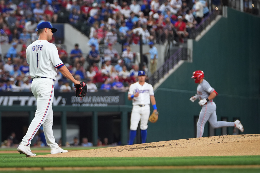 Texas Rangers starting pitcher MacKenzie Gore, left, looks on as Cincinnati Reds' Spencer Steer, right, runs the bases after hitting a two-run home run off him during the second inning of the Rangers' home-opener baseball game Friday, April 3, 2026, in Arlington, Texas. (AP Photo/Julio Cortez)