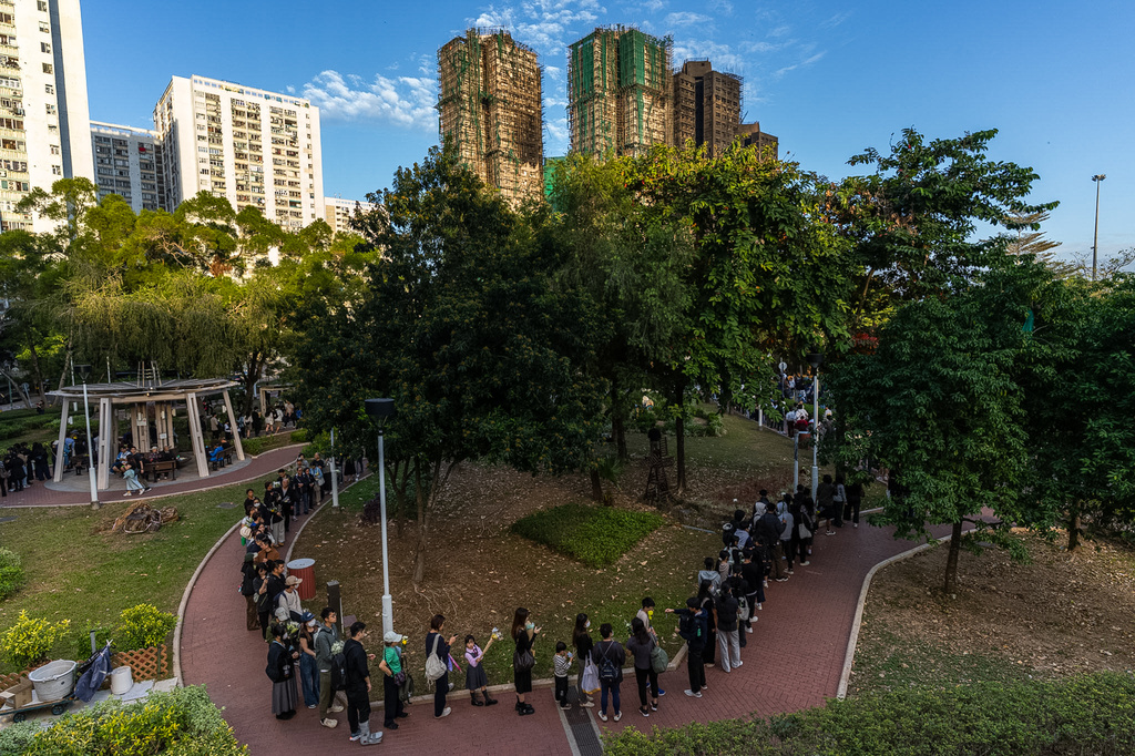 People holds flower and line up near the site to mourn the victims of the deadly Wednesday fire at Wang Fuk Court, a residential estate in the Tai Po district of Hong Kong's New Territories on Saturday, Nov. 29, 2025. (AP Photo/Chan Long Hei)