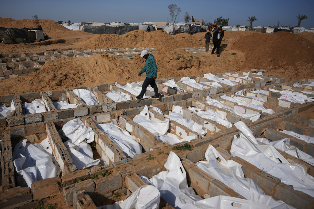 A man walks past graves containing the bodies of unidentified Palestinians returned from Israel as part of the ceasefire deal during their burial in Deir al-Balah, Gaza Strip, Friday, Feb. 13, 2026. (AP Photo/Abdel Kareem Hana)
