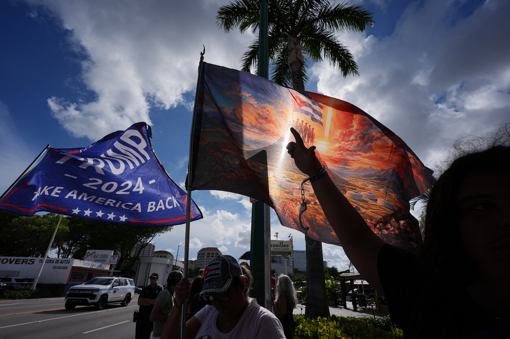 Jose Miguel Hernandez, 14, right, wears handcuffs to represent freedom for political prisoners and a call to put former Cuban President Raul Castro in jail, while his mother Catalina Vasquez waves a flag depicting Cuban political prisoners atop a mountain overlooking prisons below, hours after federal prosecutors announced charges against Castro in the 1996 downing of civilian planes operated by Miami-based exiles, Wednesday, May 20, 2026, in Miami. (AP Photo/Rebecca Blackwell)