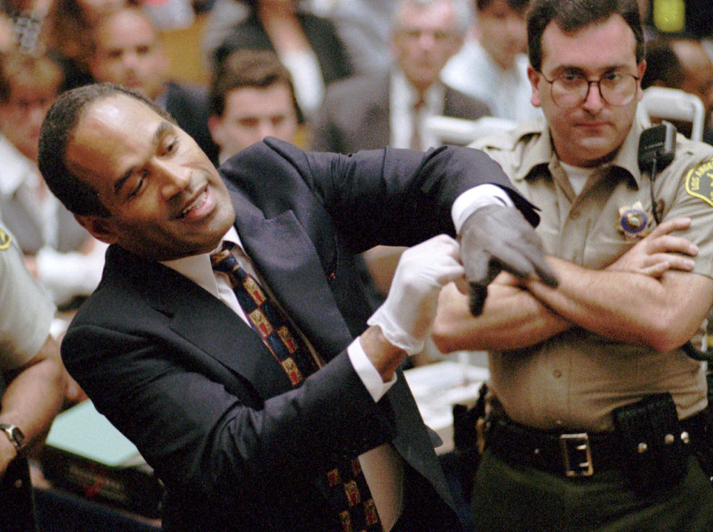 FILE - In this June 15, 1995 file photo, O.J. Simpson, left, grimaces as he tries on one of the leather gloves prosecutors say he wore the night his ex-wife Nicole Brown Simpson and Ron Goldman were murdered in a Los Angeles courtroom. (AP Photo/Sam Mircovich, Pool, File)