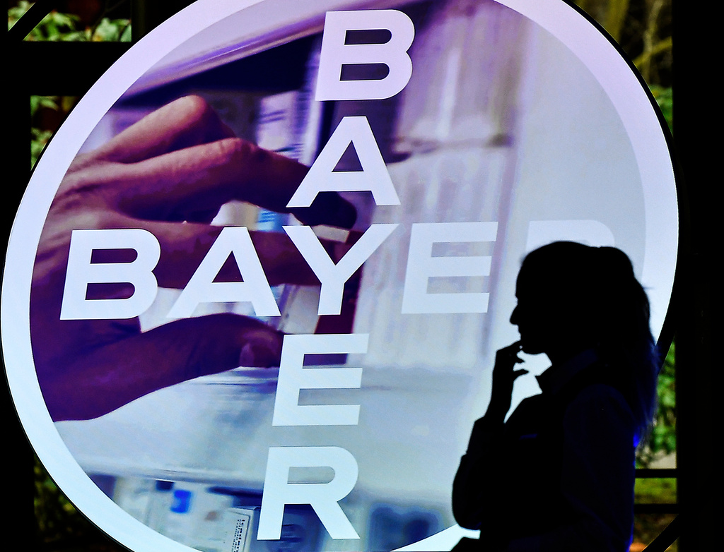 FILE - A woman walks in front of a logo of Bayer AG at the Financial News Conference, in Leverkusen, Germany, Feb. 27, 2020. (AP Photo/Martin Meissner, File)