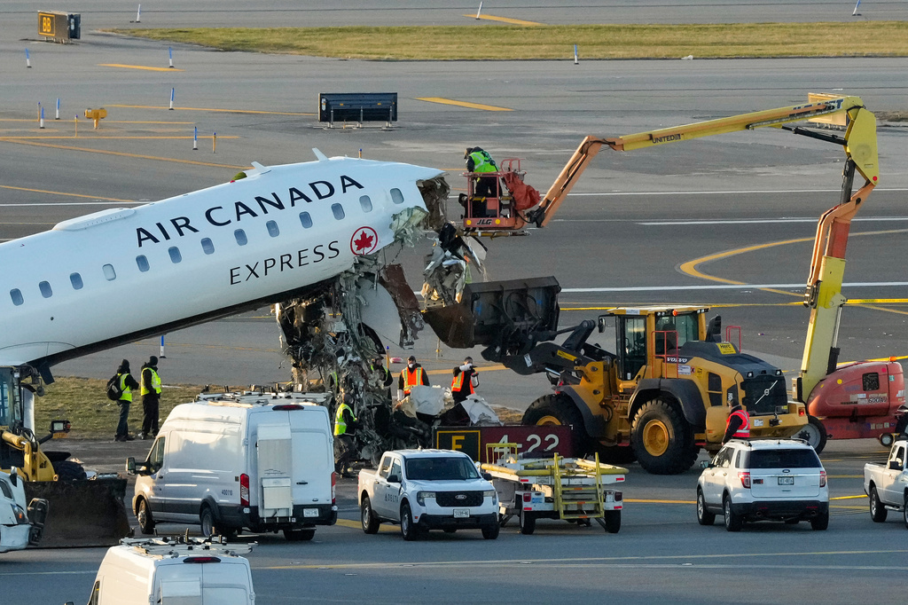 Aircraft maintenance workers in a boom lift cut away debris hanging from the wreckage of an Air Canada Express jet, Tuesday, March 24, 2026, just off the runway where it had collided with a Port Authority fire truck Sunday night at LaGuardia Airport in New York. (AP Photo/Yuki Iwamura)
