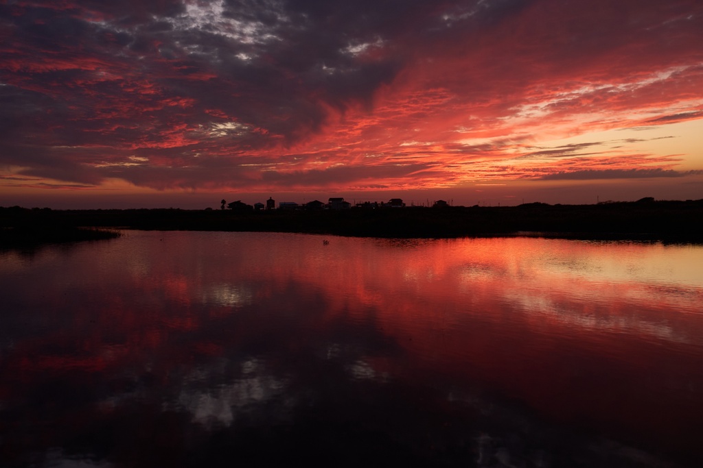 Clouds illuminated by the setting sun are reflected in water at the Wolfberry Whooping Crane Sanctuary, Friday, Dec. 12, 2025, near Seadrift, Texas. (AP Photo/John Locher)