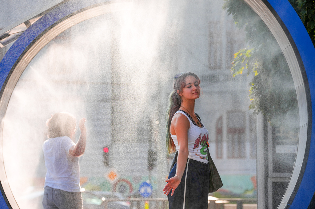FILE - A woman pauses while she walks through a water mist machine installed by city administration to assist people in coping with the heat in Bucharest, Romania, Aug. 6, 2026. (AP Photo/Vadim Ghirda, File)