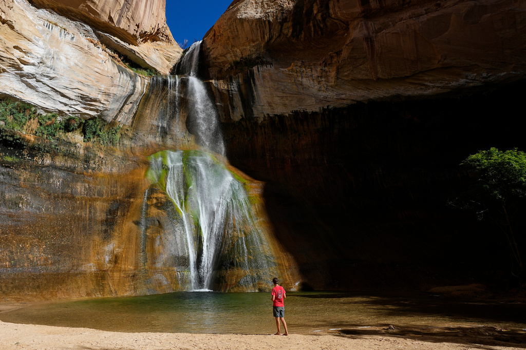FILE - A hiker watches a waterfall at Lower Calf Creek Falls at Grand Staircase Escalante National Monument, July 12, 2023, in Escalante, Utah. (AP Photo/Ross D. Franklin, File)