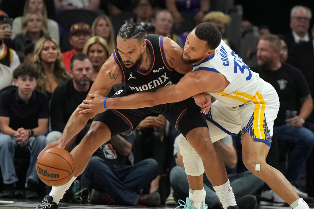 Phoenix Suns forward Dillon Brooks, left, shields the ball from Golden State Warriors guard Stephen Curry, right, during the first half of an NBA basketball play-in tournament game, Friday, April 17, 2026, in Phoenix. (AP Photo/Rick Scuteri)