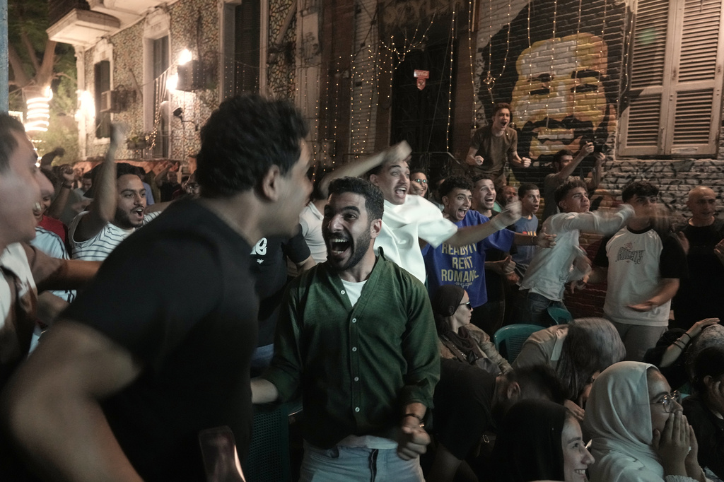 Fans celebrate after Egypt scored the first goal as they watch a broadcast of the World Cup soccer match between Egypt and Belgium at a coffee shop in Cairo, Egypt, Monday, June 15, 2026. Background graffiti shows Egyptian soccer star, Mohamed Salah. (AP Photo/Amr Nabil)