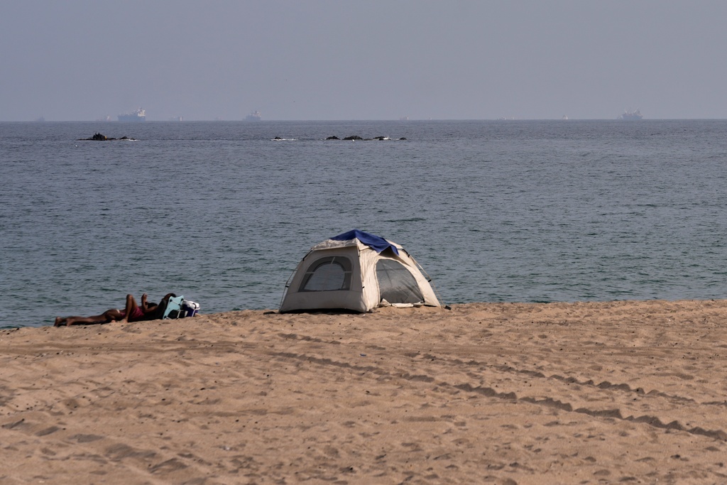 A group of people camp on a beach overlooking the Strait of Hormuz, with oil tankers and cargo ships in the background, near Khor Fakkan, United Arab Emirates, Wednesday, March 11, 2026. (AP Photo/Altaf Qadri)