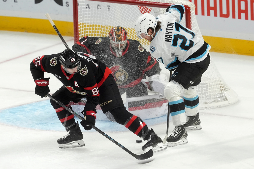 Ottawa Senators goaltender Leevi Merilainen (1) keeps his eye on the puck Utah Mammoth centre Barrett Hayton (27) stick handles the puck past defenceman Jake Sanderson (85) during first period NHL action, in Ottawa, Sunday, Nov. 9, 2025. (Adrian Wyld/The Canadian Press via AP)