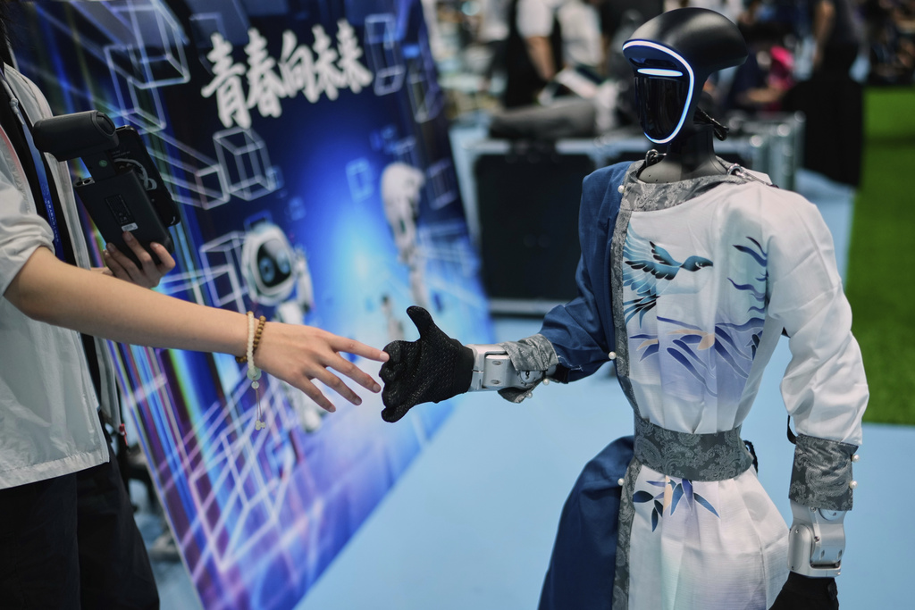 A woman touches the hand of a robot that performed in the dance event at the World Humanoid Robot Games Beijing, China, Saturday, Aug. 16, 2025. (AP Photo/Mahesh Kumar A.)