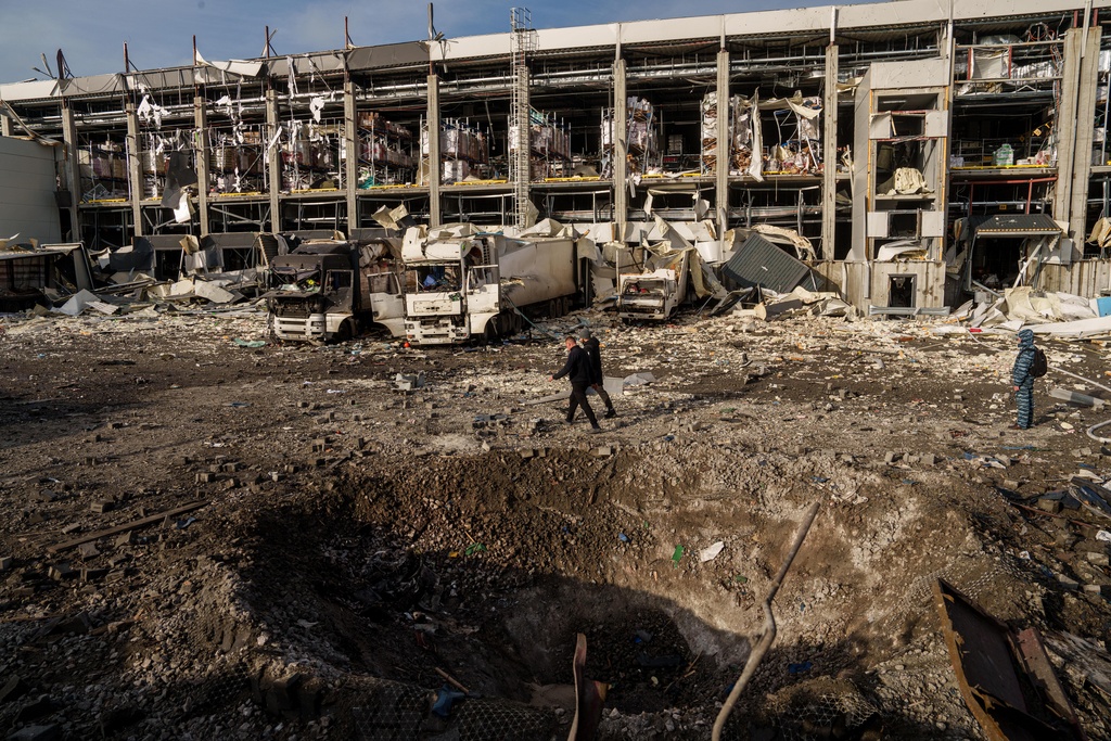 Police officers walk near a crater in front of a Novus logistics center damaged after a Russian strike on Kyiv, Ukraine, on Tuesday, Nov. 25, 2025. (AP Photo/Evgeniy Maloletka)