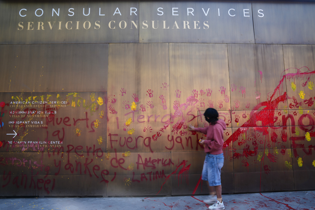 A woman defaces the facade of the U.S. Embassy with red handprints in protest against the capture of President Nicolas Maduro, in Mexico City, Saturday, Jan. 3, 2026. (AP Photo/Marco Ugarte)
