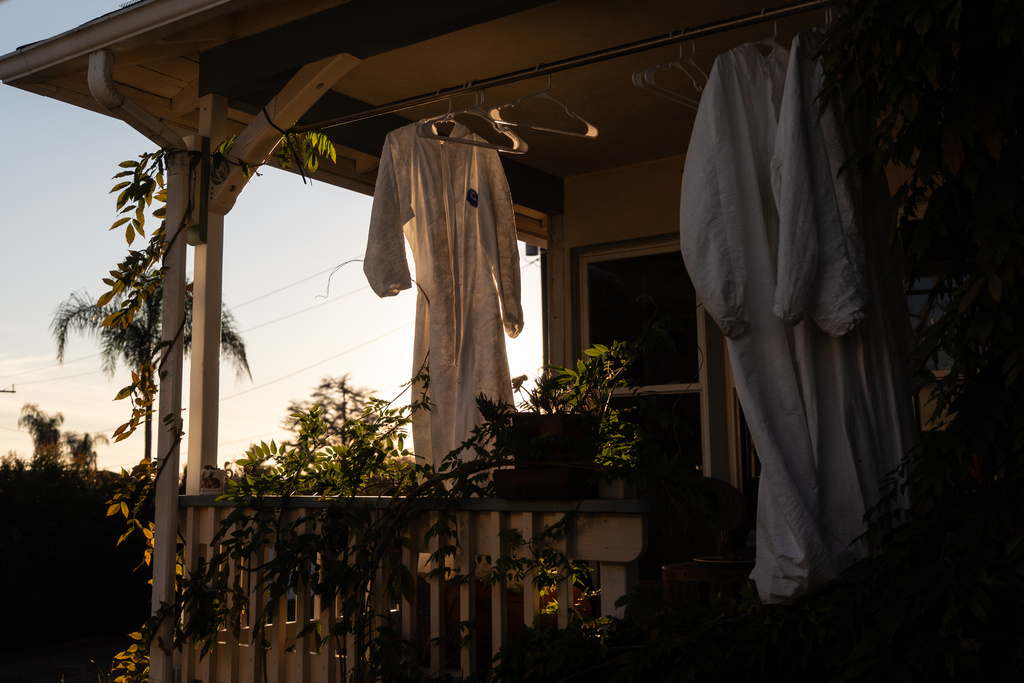 Protective suits hang outside a home that survived the Eaton Fire, Dec. 2, 2025, in Altadena, Calif., as cleaning crews remove fire debris from the property. (AP Photo/Jae C. Hong)