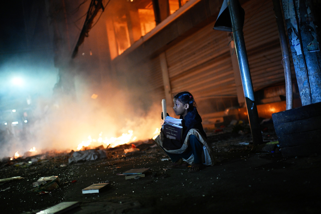 FILE - A girl rescues books from a shop near the Prothom Alo daily newspaper which was set on fire by protesters after news reached the country from Singapore of the death of a prominent activist Sharif Osman Hadi, in Dhaka, Bangladesh, Dec. 19, 2025. (AP Photo/Mahmud Hossain Opu, File)