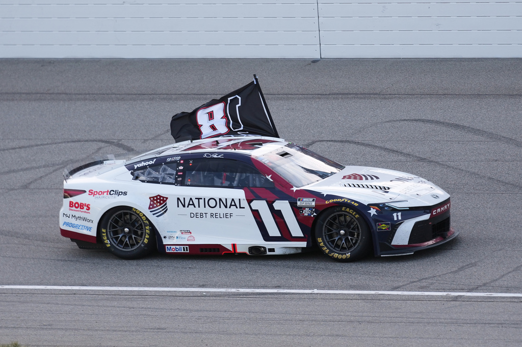 Denny Hamlin celebrates winning while honoring Kyle Busch with a flag after a NASCAR Cup Series auto race at Michigan International Speedway in Brooklyn, Mich., Sunday, June 7, 2026. (AP Photo/Paul Sancya)