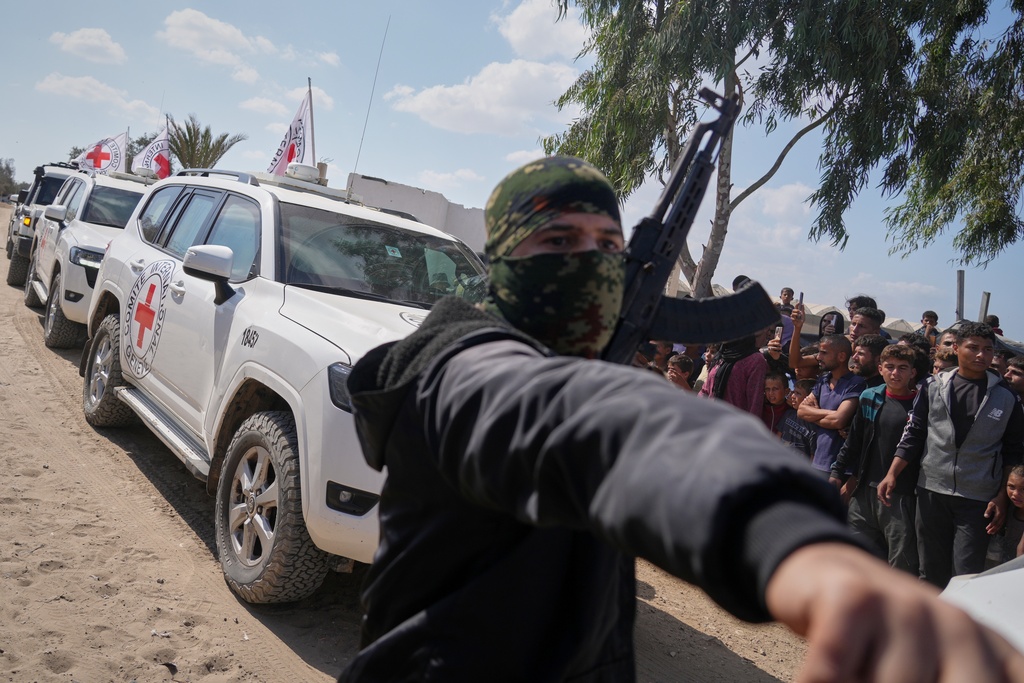ICRC vehicles carrying released Israeli hostages make their way through groups of Palestinians and Hamas gunmen on their way to the Israeli border, in Khan Younis, southern Gaza Strip, Monday, Oct. 13, 2025. (AP Photo/Jehad Alshrafi)