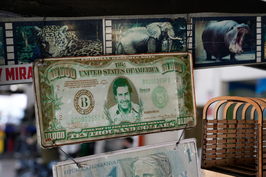 A plaque made from a dollar bill bearing the face of the late drug trafficker Pablo Escobar is displayed alongside photographs of wildlife at a souvenir store in Puerto Triunfo, Colombia, Thursday, April 23, 2026. (AP Photo/Fernando Vergara)