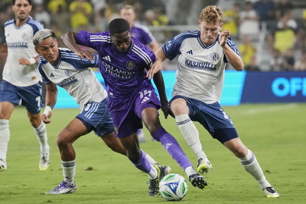Orlando City forward Tyrese Spicer, center, moves the ball past Nashville SC midfielder Andy Najar, left, and forward Jacob Shaffelburg, right, during the first half of an MLS soccer match Saturday, Aug. 23, 2025, in Nashville, Tenn. (AP Photo/George Walker IV)