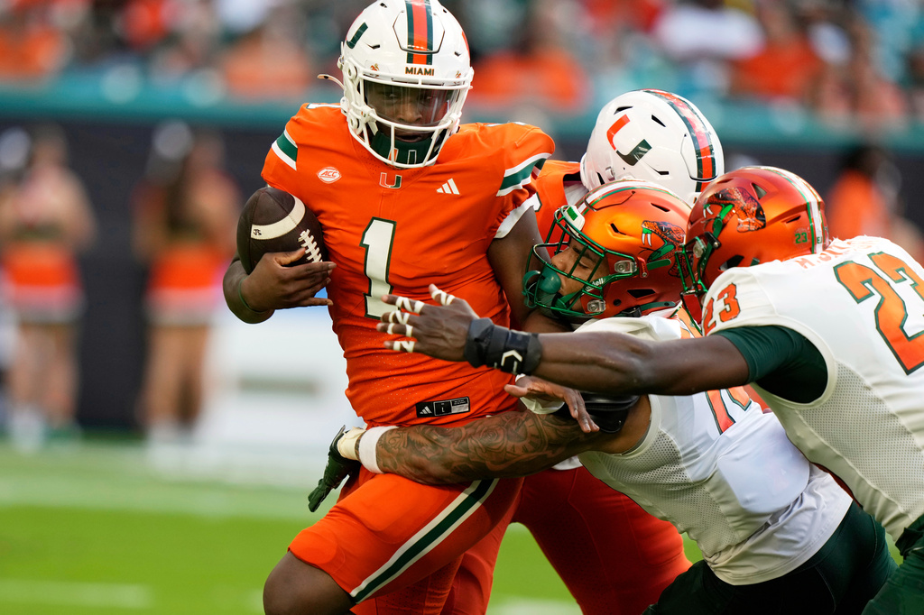 FILE - Miami quarterback Cam Ward (1) is defended by Florida A&M defensive back Simion Hines, center, and defensive lineman Allen Smith Jr. (23) during the first half of an NCAA football game, Sept. 7, 2024, in Miami Gardens, Fla. (AP Photo/Lynne Sladky, File)