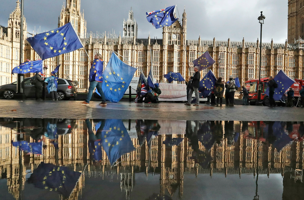 FILE - Protestors are reflected in a large puddle as they wave European flags to demonstrate against Brexit in front of the Parliament in London, Dec. 3, 2018. (AP Photo/Frank Augstein, File)