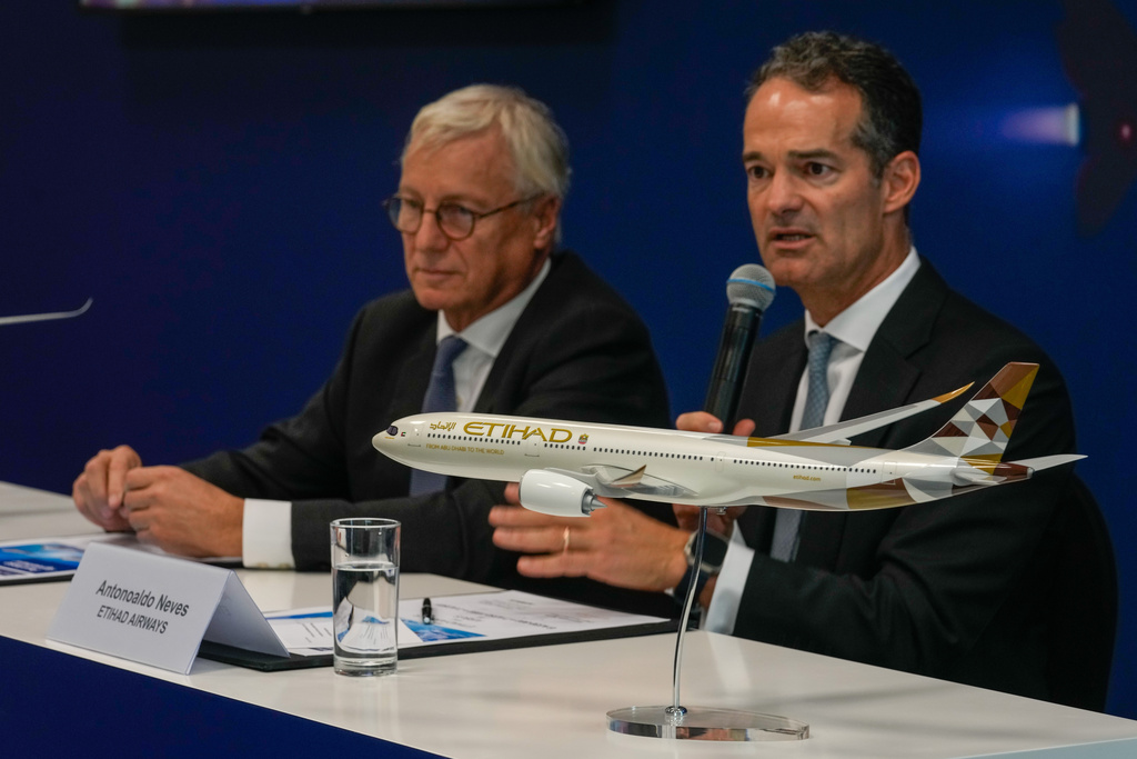 A model of Airbus A350 sits on the table as Etihad Airways CEO Antonoaldo Neves speaks while Airbus' CEO of commercial aircraft Christian Scherer, left, looks on during a press conference to announce deal to purchase 16 Airbus planes at the Dubai Air Show, United Arab Emirates, Tuesday, Nov. 18, 2025. (AP Photo/Altaf Qadri)