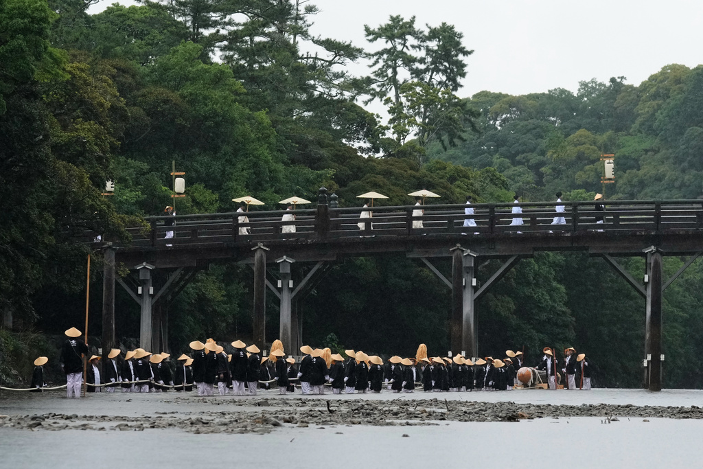 Shinto priests and officials in the priesthood walk on the Uji bridge, as people pull a sacred timber in the Isuzu river towards Kotaijingu, also known as Naiku, or the inner sanctuary of the Ise Jingu shrine complex, during the Mihishirogi Hoeishiki ceremony of the Shikinen Sengu ritual to rebuild its main structures for Shinto deities, in Ise, central Japan, Monday, June 9, 2025. (AP Photo/Hiro Komae)