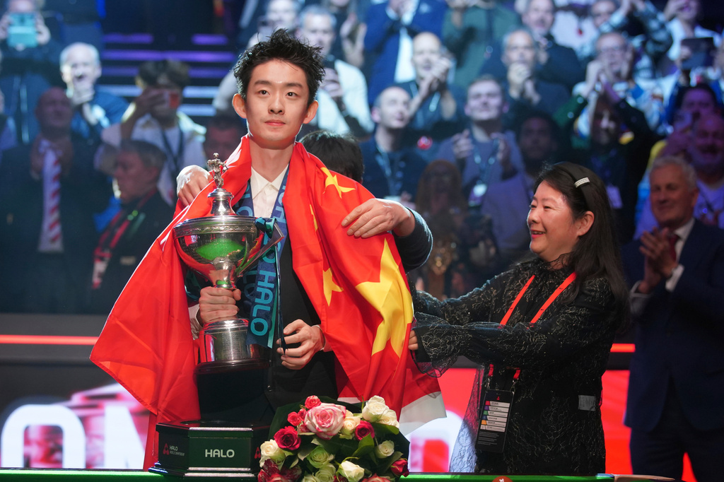 China's Wu Yize poses for the media with the trophy and wearing the Chinese national flag, after winning the World Snooker Championship defeating England's Shaun Murphy in Sheffield, England, Monday, May 4, 2026.(AP Photo/Ian Hodgson)